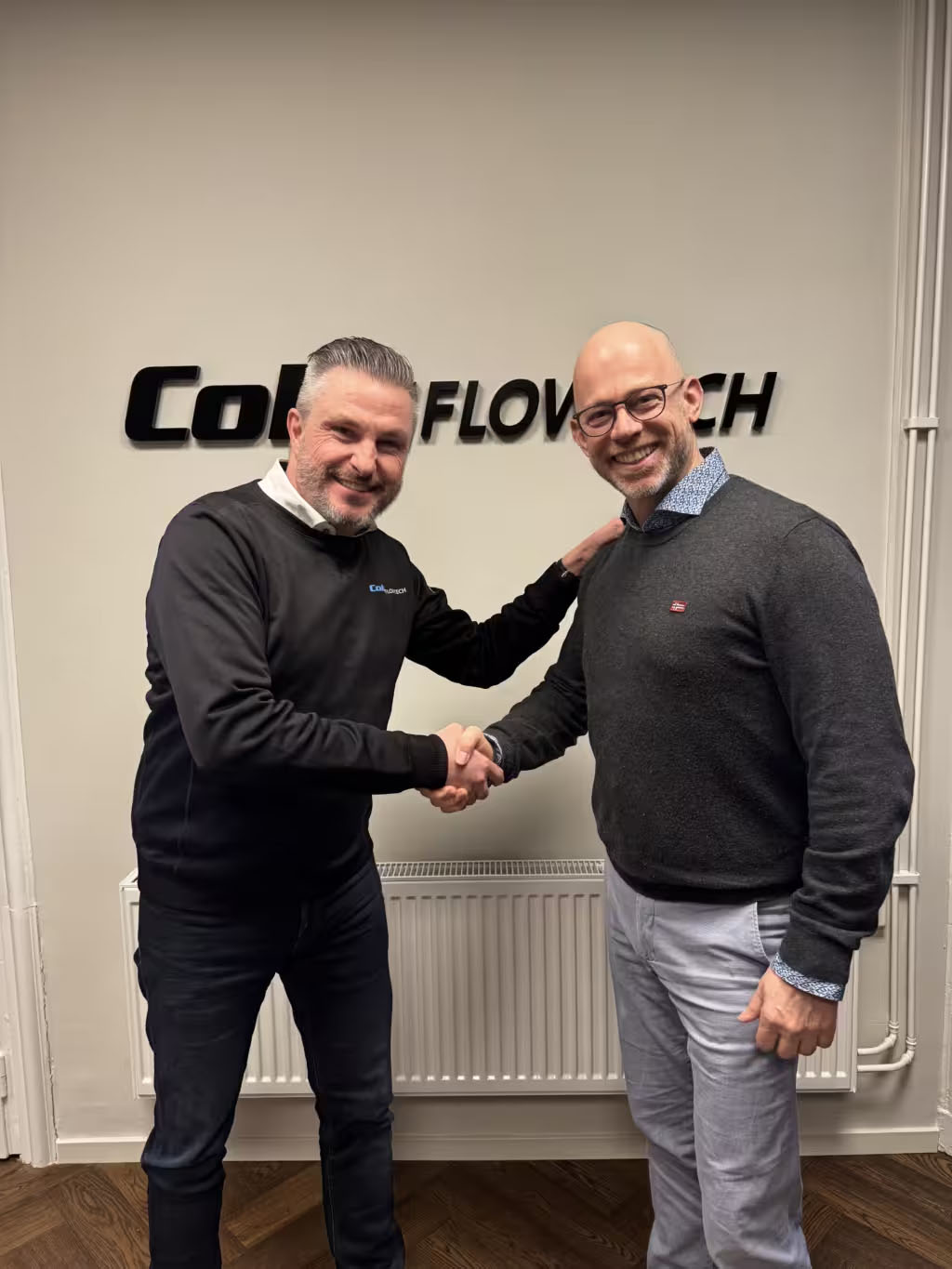 Tvä män som skakar hand framför en colly flowtech skylt