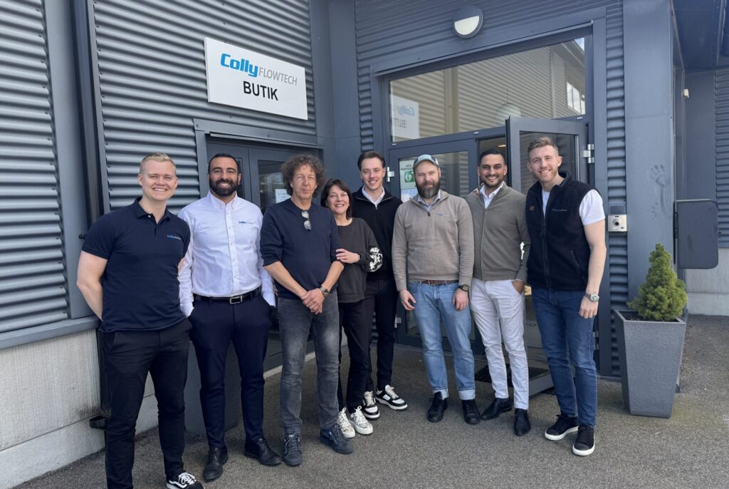 Representatives from Colly Flowtech and Fluortubing stand together in front of the entrance, smiling at the camera.