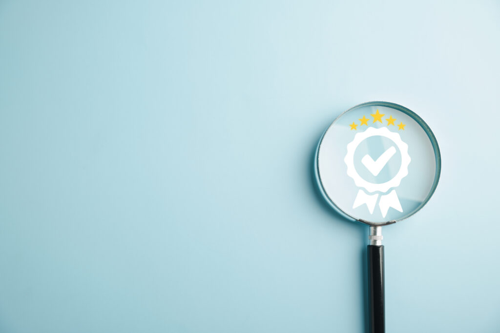 Förstoringsglas som lyfter fram en kvalitetsstämpel med checkmark – symbol för ISO 9001 och kvalitetssäkring.